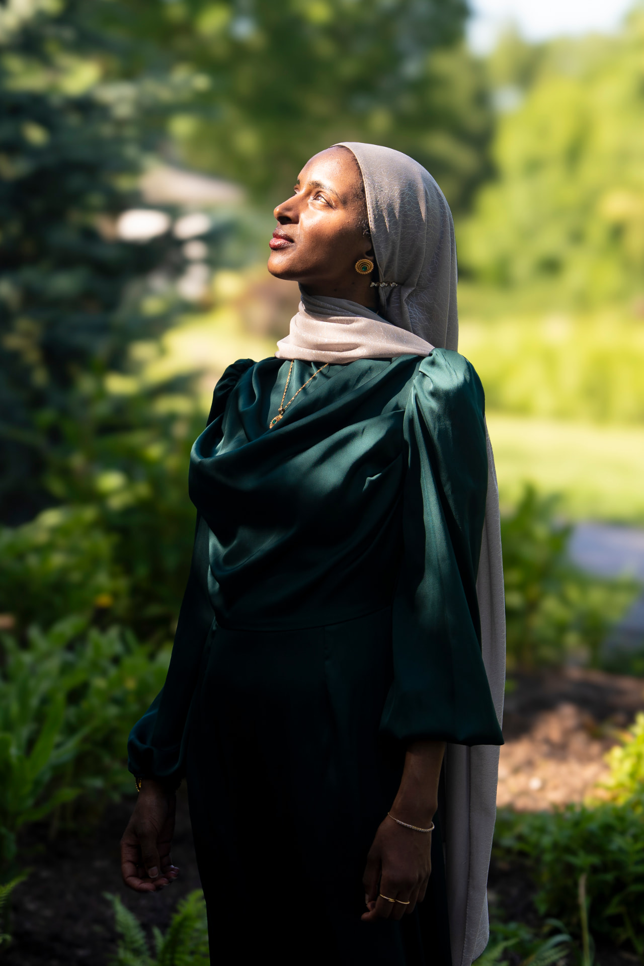 Salimah Hussien looking upward in a garden, editorial portrait