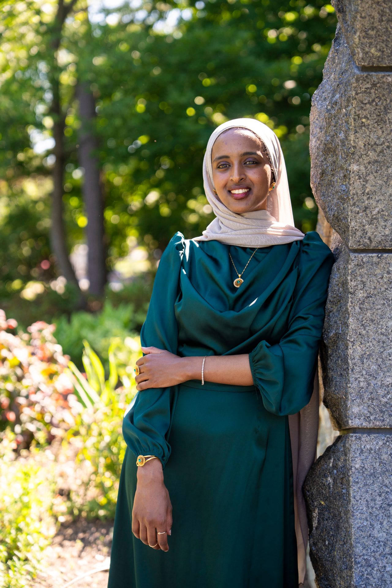 Salimah Hussien leaning against a stone wall in a sunlit garden
